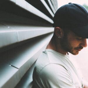 A man in a hat leaning against the wall.