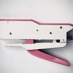 A pink and white stapler on top of a table.