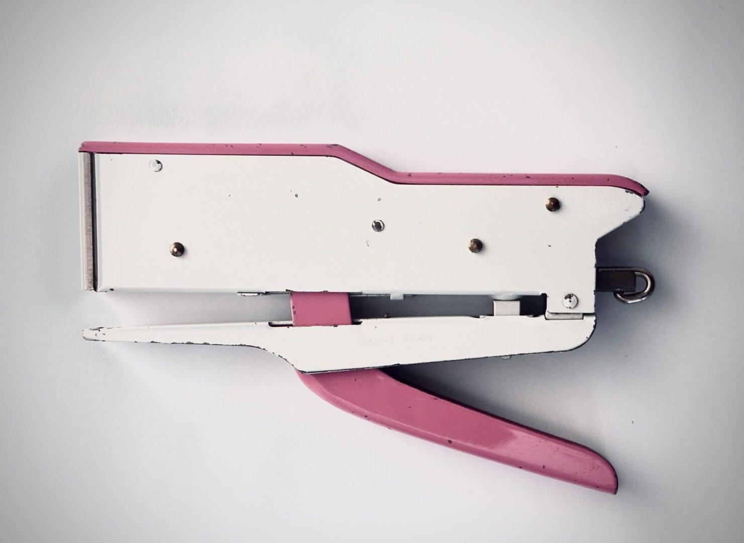 A pink and white stapler on top of a table.